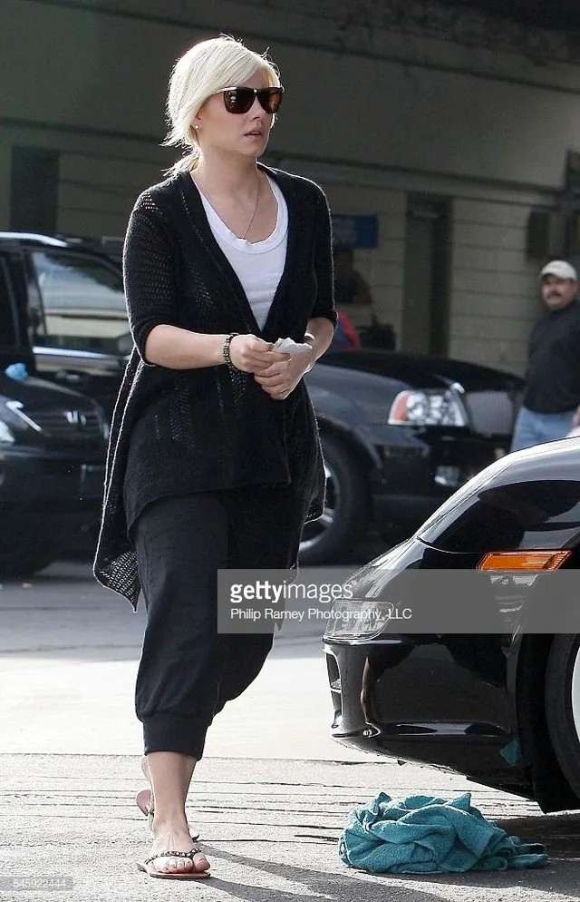 Elisha Cuthbert walking beside a car in cropped trousers and flip-flops.