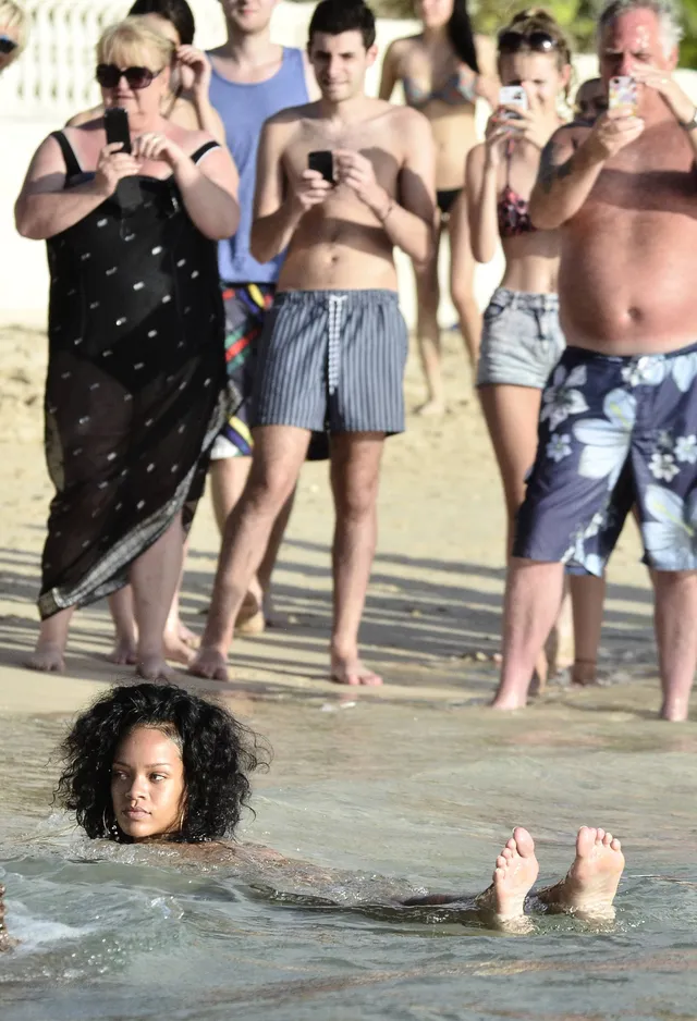 Rihanna swimming beside a beach with bare soles raised.
