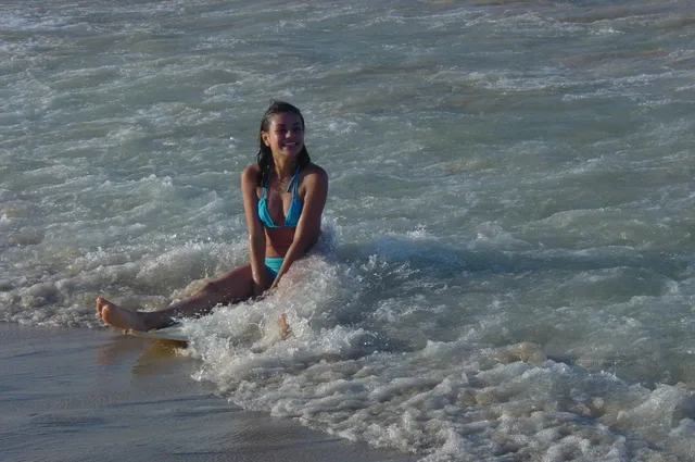 Mila Kunis sitting barefoot in shallow seawater.