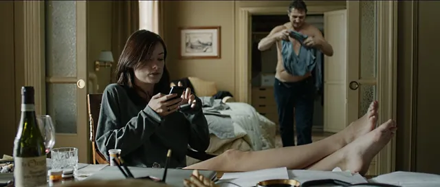 Olivia Wilde reclining on a bed with her bare feet extended in a film scene.