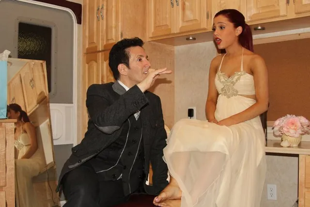 Ariana Grande performing indoors in a cream-colored dress and pointed heels.