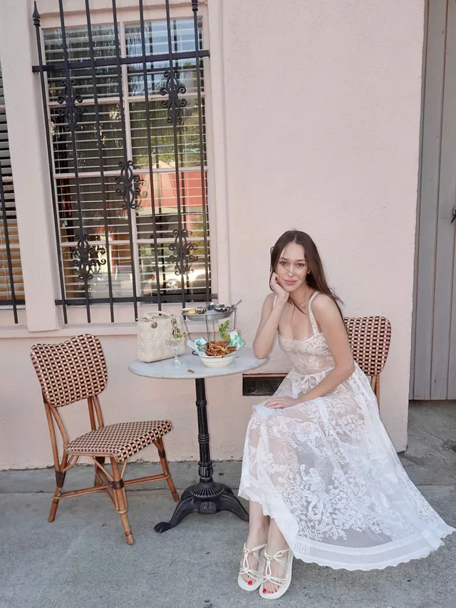 Alycia Debnam-Carey sitting on a patio chair in a white lace dress.