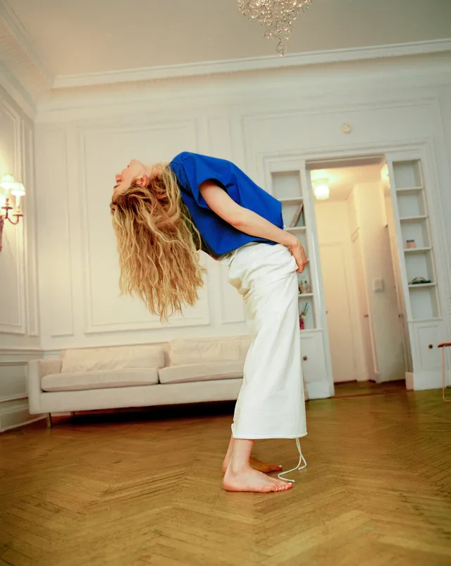 Sarah Pidgeon posing barefoot in a blue top and white trousers.