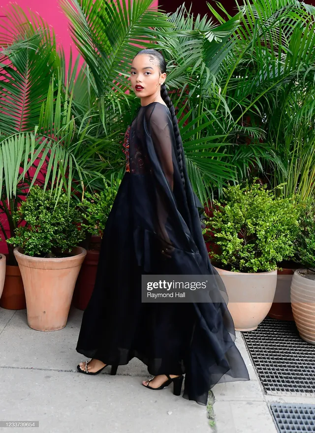 Whitney Peak posing by palm plants in a dark skirt and black heels.
