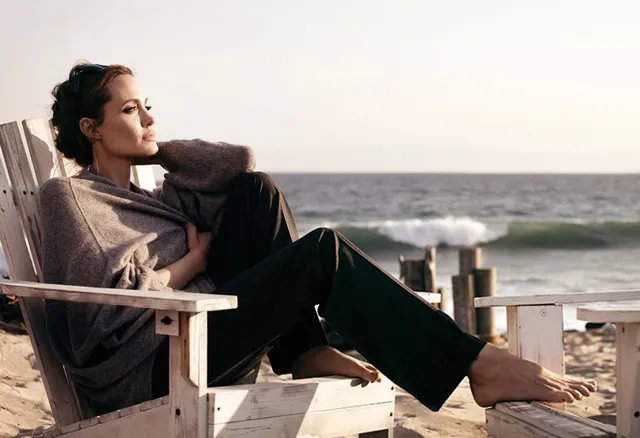 Angelina Jolie seated in a wooden chair beside the sea.