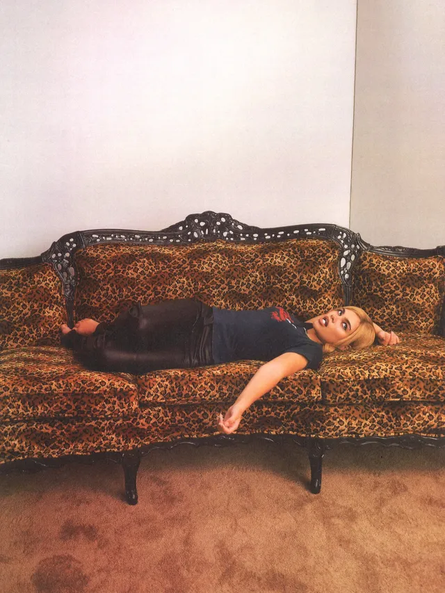 Ariana Greenblatt reclining barefoot on a patterned sofa.