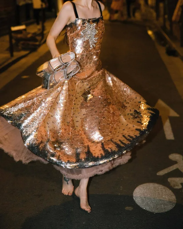 Dove Cameron twirling barefoot in a shimmering dress outside.