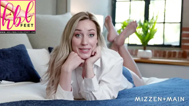 Paige Spiranac lying on a bed with her bare feet raised behind her.
