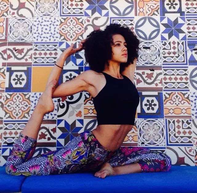 Nathalie Emmanuel stretching on a blue cushion beside a patterned wall.
