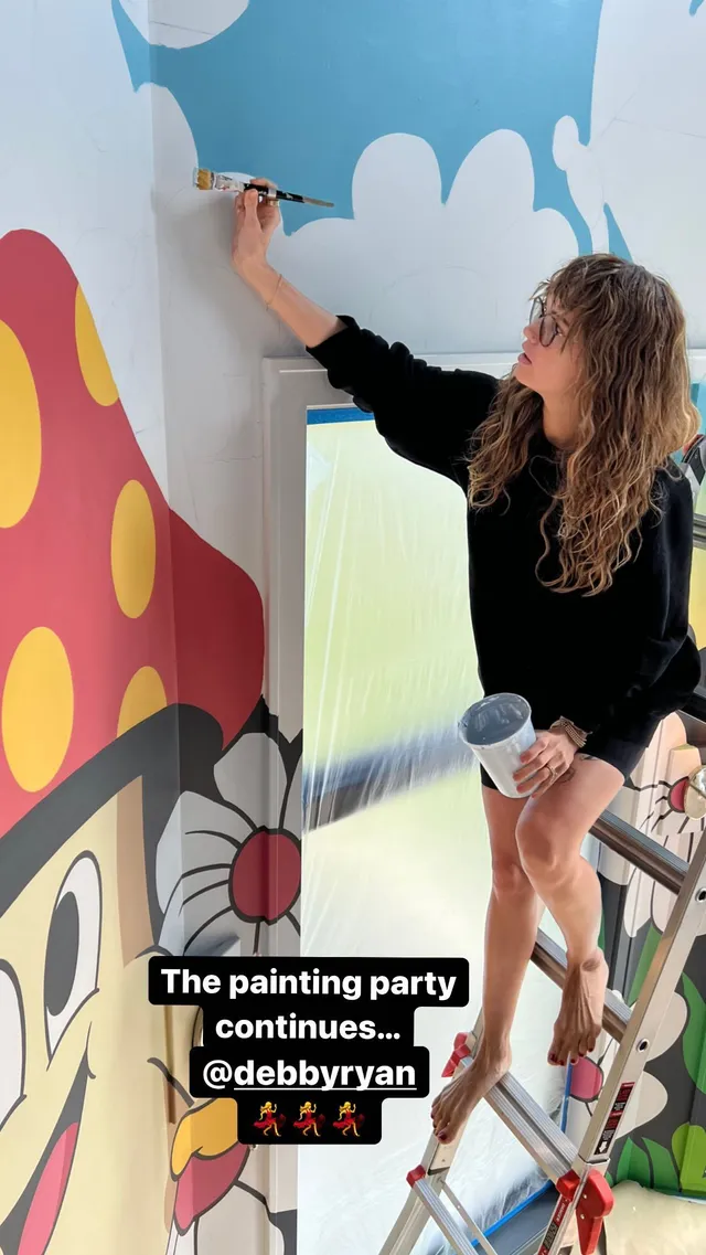 Debby Ryan painting a colorful wall while standing on a ladder.