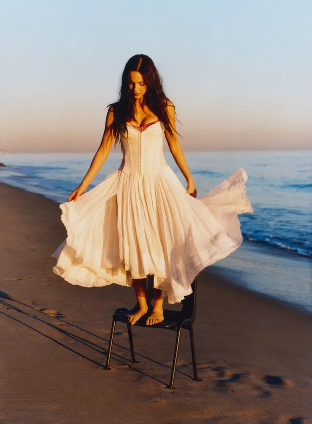 Olivia Rodrigo posing beside the sea in a flowing dress.