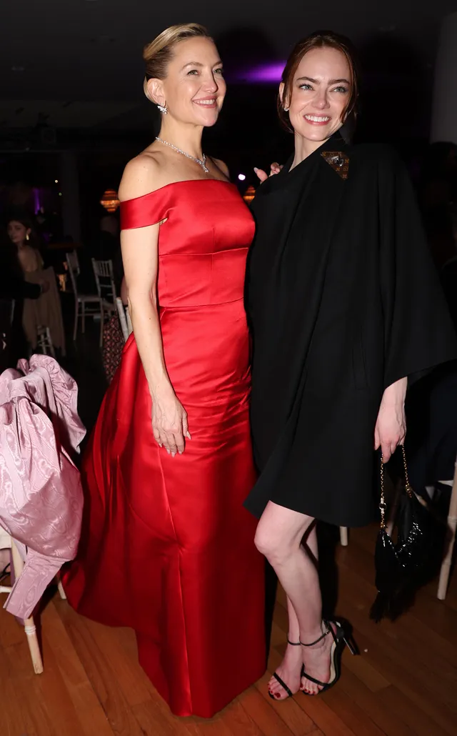 Emma Stone smiling beside another guest in a black dress and strappy heels.