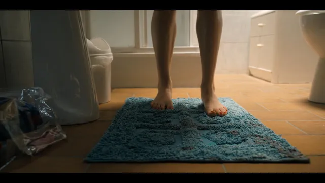 Grace Van Patten stepping barefoot on a blue bathroom mat.