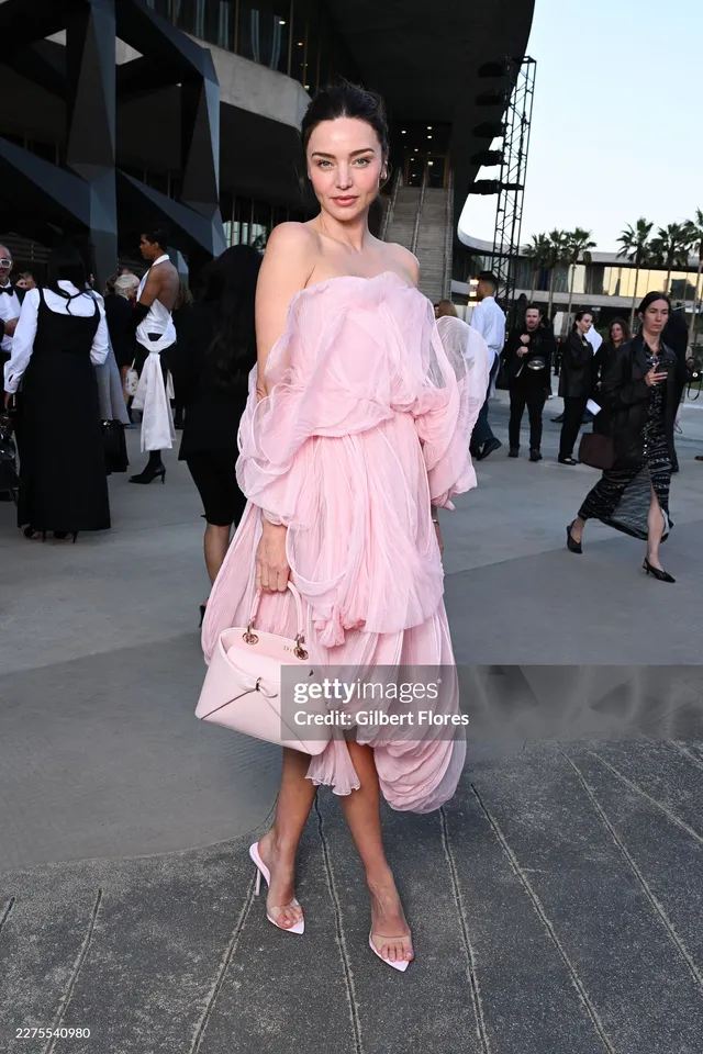 Miranda Kerr a pink dress and white heels outdoors.