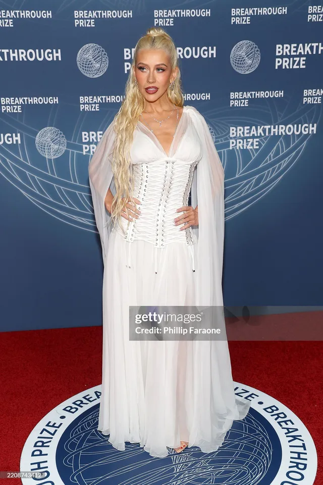 Christina Aguilera standing on a red carpet in a long white gown.