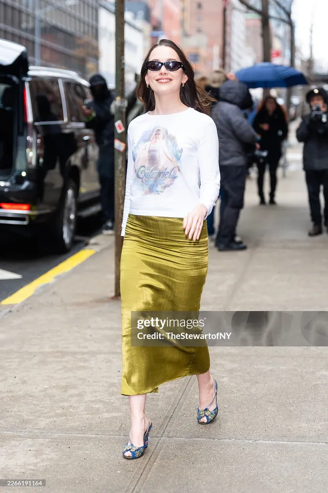 Victoria Pedretti walking on a pavement in a white top and green skirt.