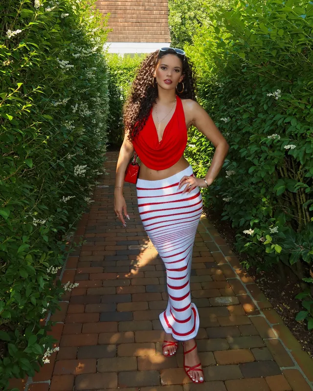 Madison Pettis posing outdoors in a red top, striped skirt and red heels.