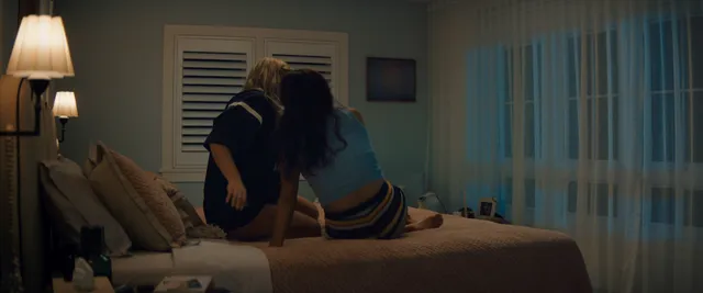 Chase Sui Wonders sitting beside a companion on a bed in a scene.