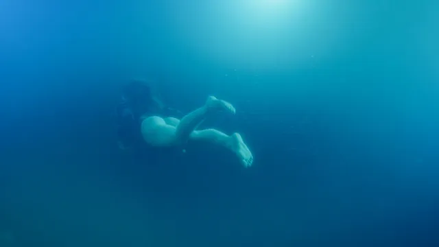 Odessa A'zion swimming underwater in a dimly lit scene.