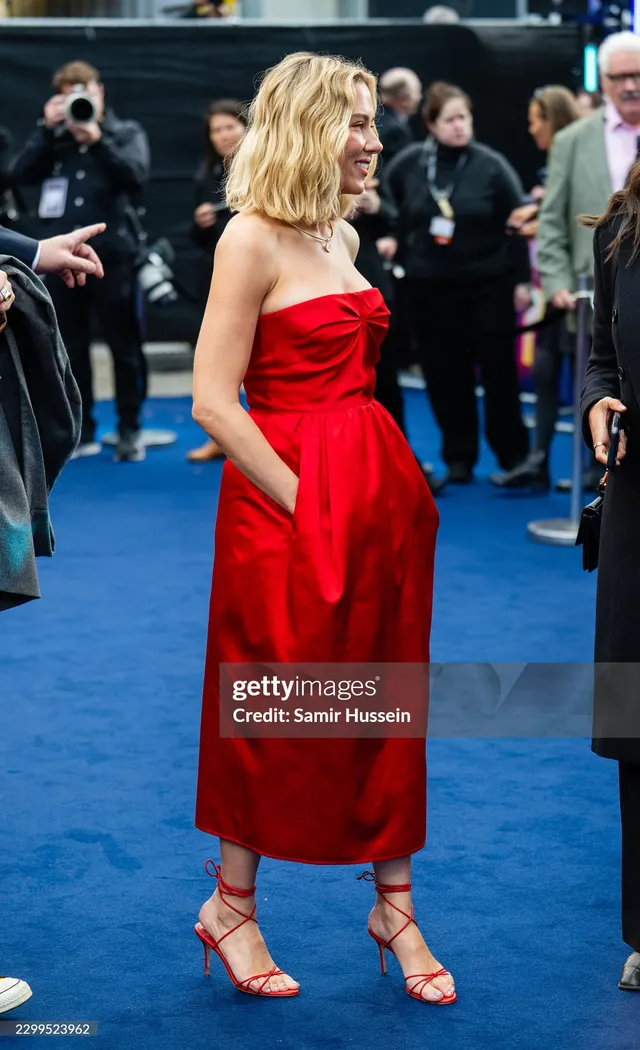 Scarlett Johansson standing among guests in a red dress and heels at a film event.
