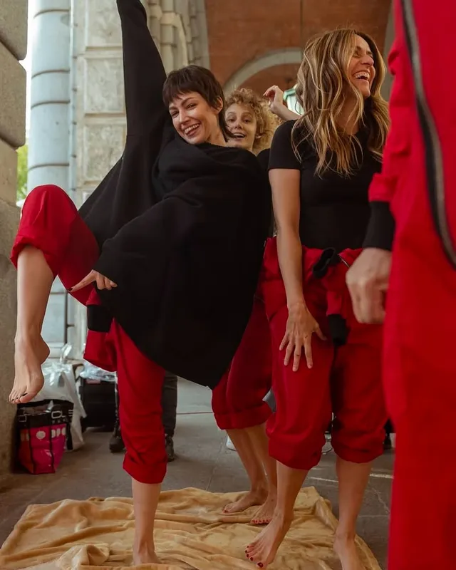 Úrsula Corberó posing barefoot with friends in red and black outfits indoors.