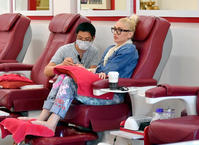 Gwen Stefani sitting at a nail salon with bare feet resting on a towel.