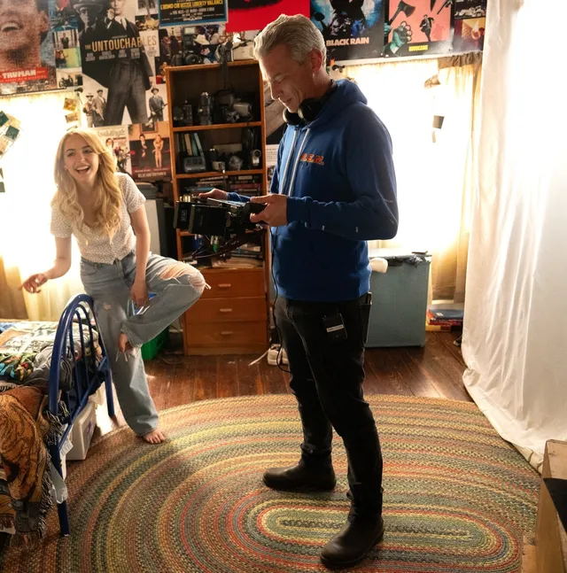 Mckenna Grace sitting beside another person among bookshelves in jeans.