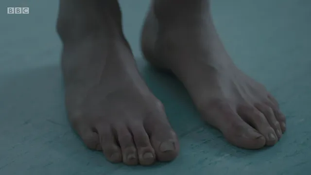 Jodie Comer standing on a pale floor in a screen scene.