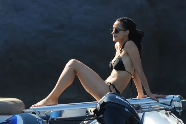 Nathalie Emmanuel sitting on a small boat in black swimwear.
