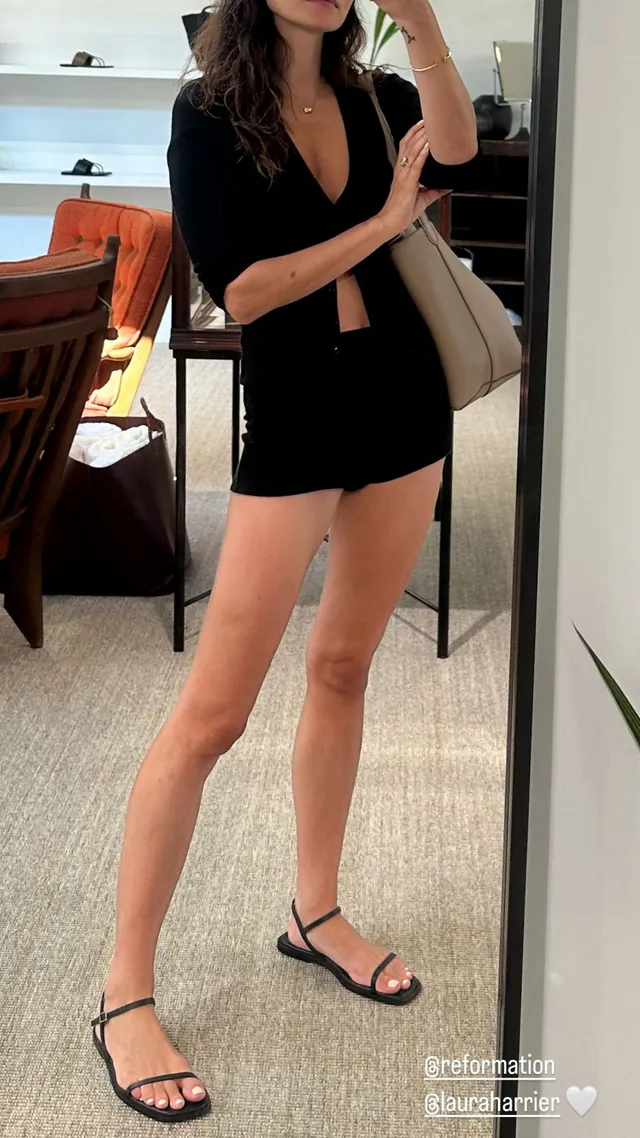 Phoebe Tonkin taking an outfit portrait in black shorts and sandals.