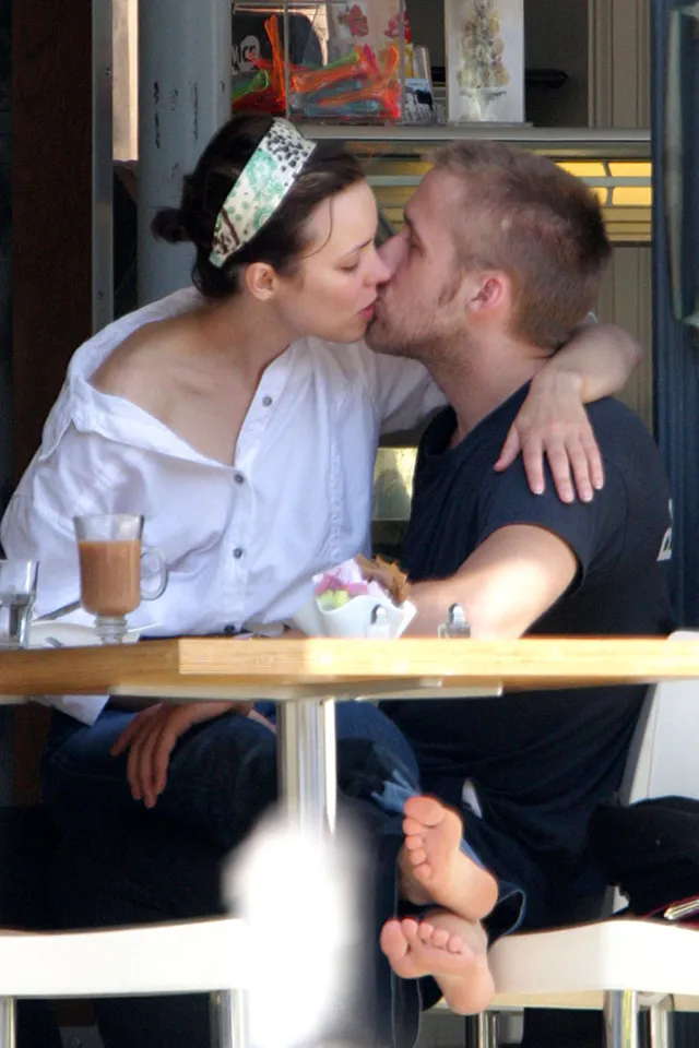 Rachel McAdams kissing another person at a café with bare soles visible.