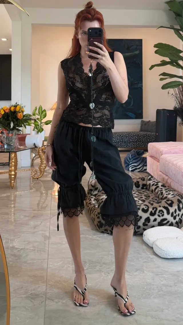 Bella Thorne posing in a black dress and heels for a mirror photo.