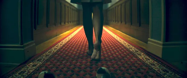 Ester Expósito walking barefoot down a patterned hallway during a screen scene.