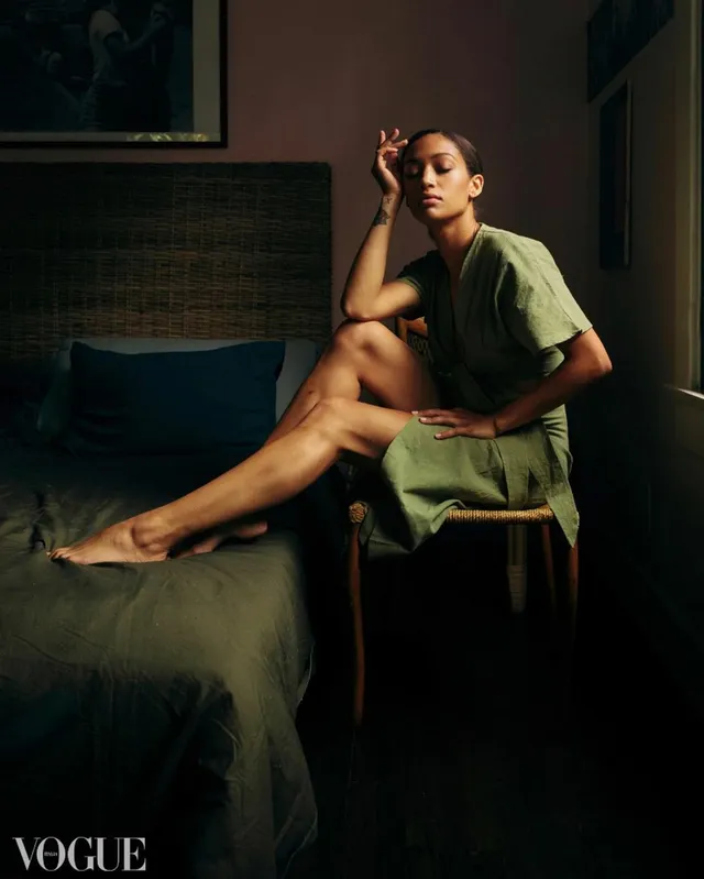 Samantha Logan sitting barefoot on a bed in a green outfit for a portrait.