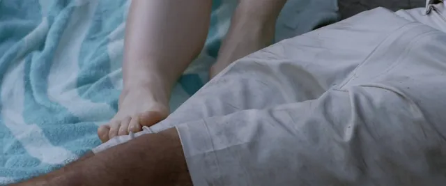 Willa Fitzgerald sitting with a bare foot on bedding in a scene.