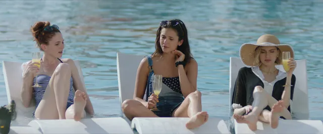 Nina Dobrev sitting barefoot with friends on a floating platform.