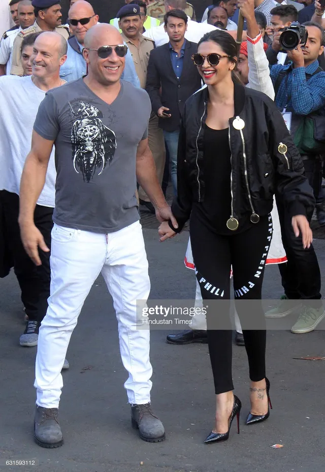 Deepika Padukone walking beside companions in black flat shoes and a dark outfit.