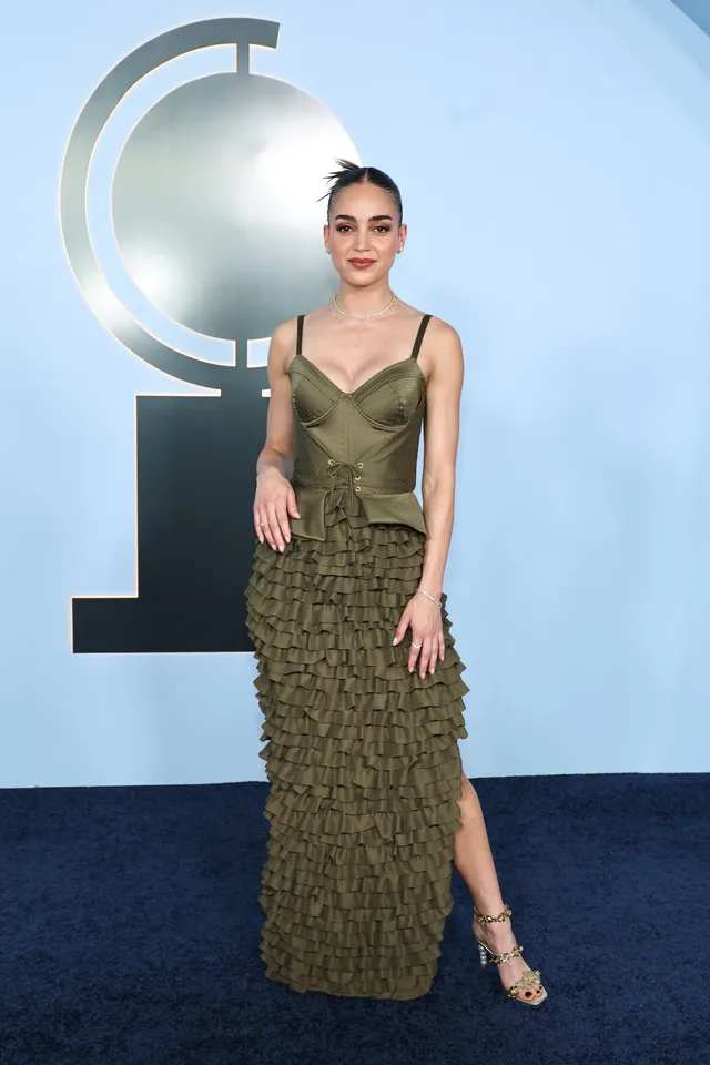 Melissa Barrera wearing an olive gown and embellished heels at an event.