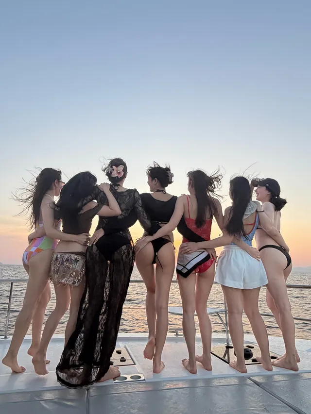 Lisa (Lalisa Manobal) standing barefoot with companions on a terrace at sunset.