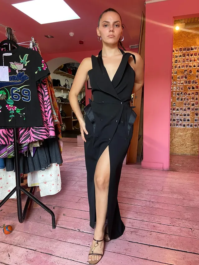 Dafne Keen posing in a black dress and heels in a pink room.