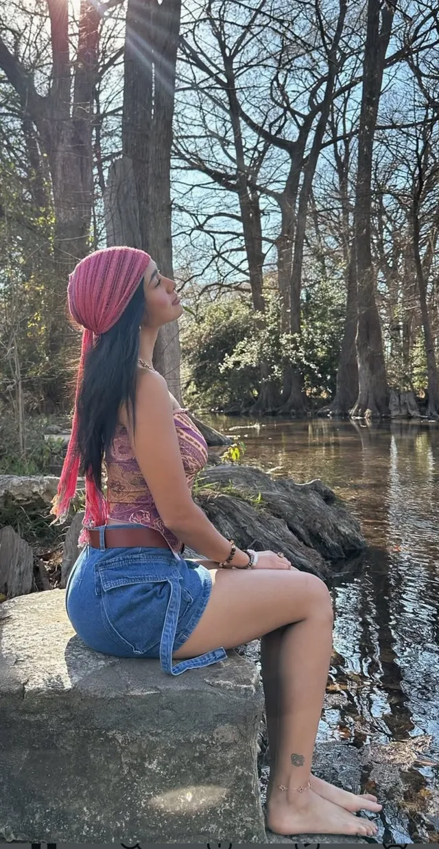 Emily Tosta sitting barefoot beside a stream.