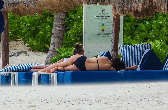 Catherine Zeta-Jones relaxing on a seaside lounge chair in a black swimsuit.