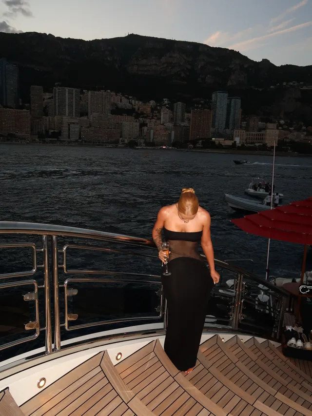 Iggy Azalea standing on a boat in a long black outfit.