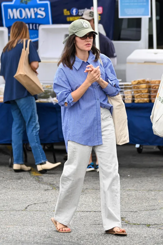Lucy Hale standing outside a shop in a blue shirt and cap.
