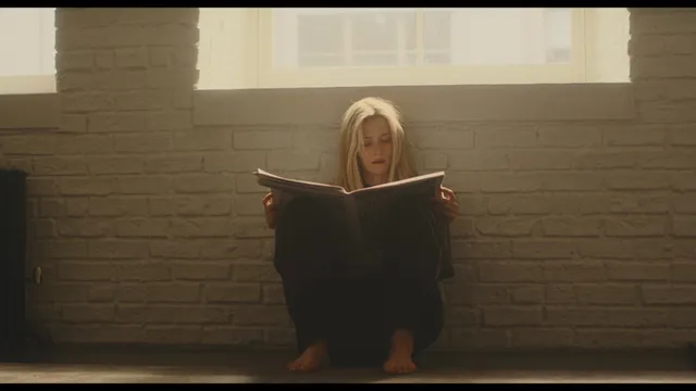 Sarah Pidgeon sitting with bare feet visible beneath a newspaper.