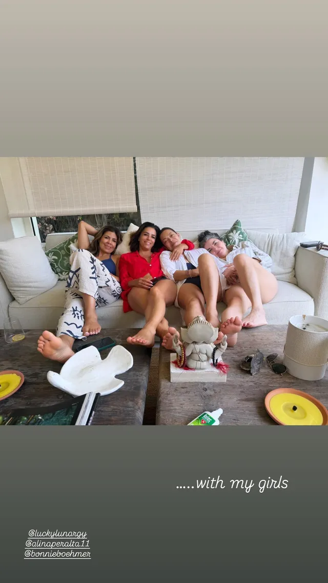 Eva Longoria sitting on a sofa with friends and bare feet raised.