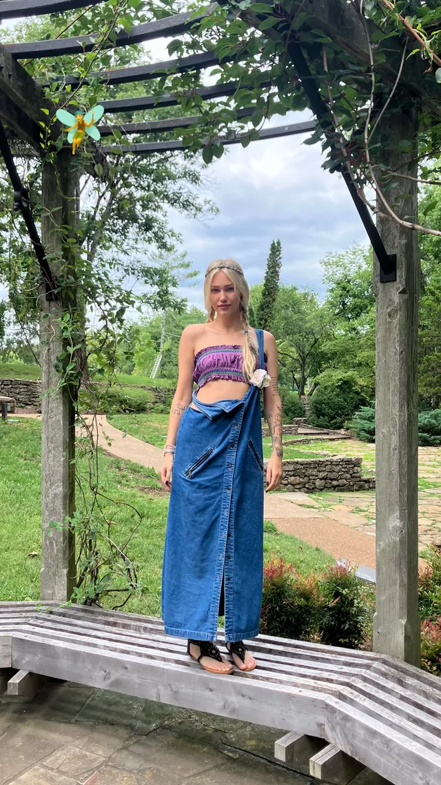 Grace VanderWaal standing beneath a garden arch in a blue skirt and heels.