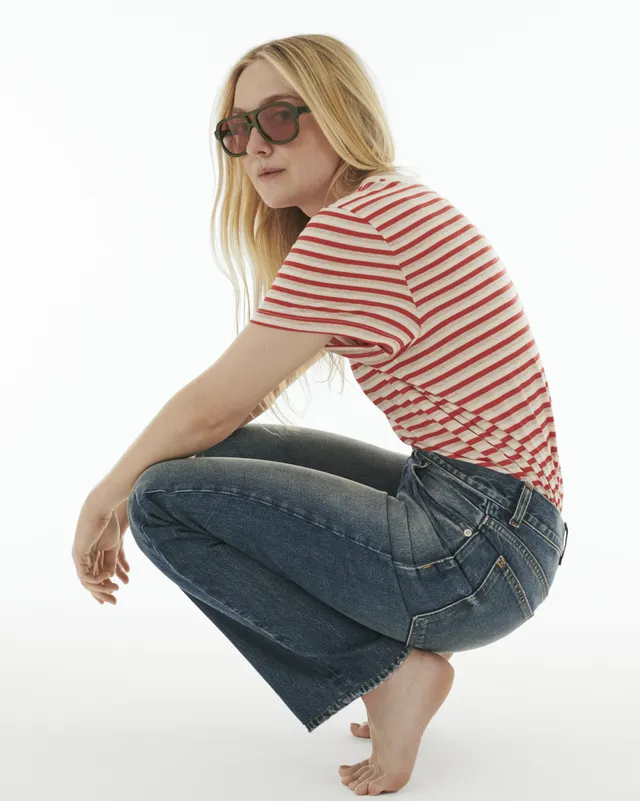 Dakota Fanning crouching barefoot in jeans and a striped shirt.