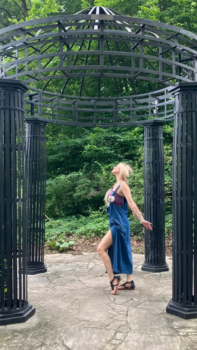 Grace VanderWaal walking beneath a garden arch in a blue skirt and heels.