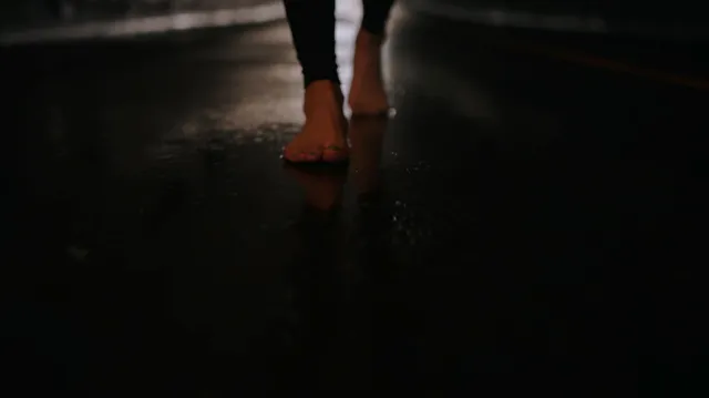 Peyton List walking barefoot across a dark floor.